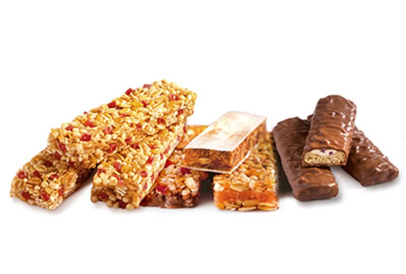 Healthy Snacks– Bienestar en el bolsillo Barritas de cereales, de fruta y de chocolate apiladas unas junto a otras.