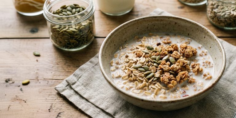 Eine Schüssel Müsli mit Milch und Kürbiskernen seht auf einem rustikalen Holztisch